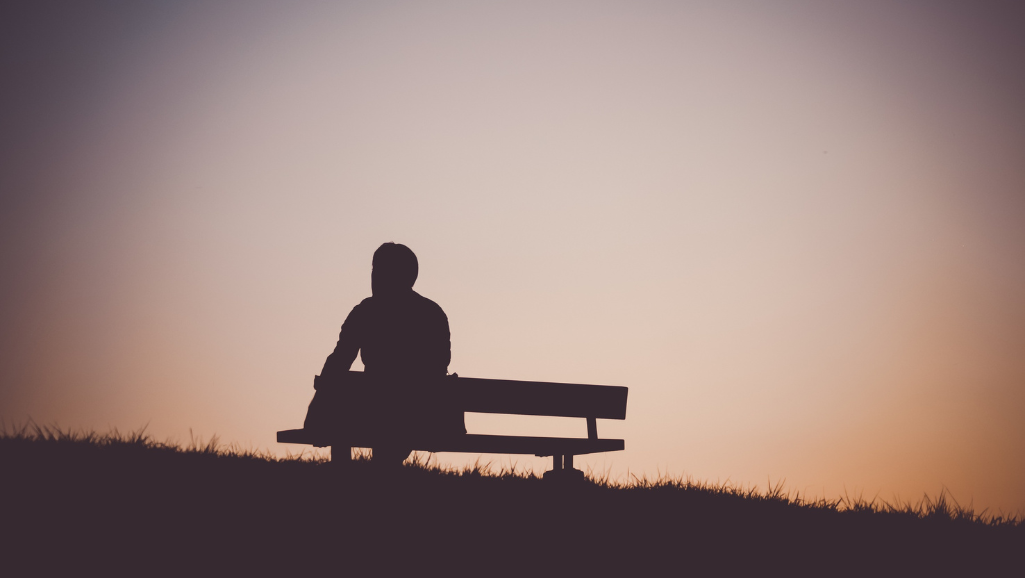 A serene scene of a person sitting on a rock, gazing out over a tranquil lake at sunset. They appear lost in contemplation, a slight smile on their face, their body language conveying a sense of inner peace and resilience. The lighting is soft and warm, creating a golden glow that envelops the figure, symbolizing the triumph over anxiety. In the background, lush, verdant hills rise up, hinting at the journey to this moment of calm. The composition is balanced, with the person centered, their reflection mirrored in the still waters below. This image evokes a sense of inspiration, resilience, and the power of personal growth in the face of life's challenges.